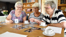 Snakken går livligt hen over kaffebordet hos Erna Kristensen, mens Tove Pedersen (t.v.), Erna Kristensen og Grethe Moesner ser på billeder fra 40 år med Hjerting Folkedansere.